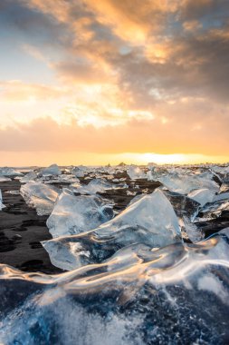Elmas Sahili üzerinde inanılmaz bir gün batımı, İzlanda 'daki Jokulsarlon buzulundan gelen buzdağlarıyla volkanik kara plaj.