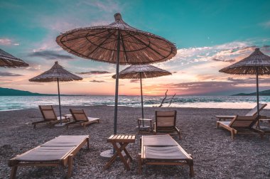 Gün batımı gökyüzü ve deniz altyapısı olan güneşli plaj şemsiyeleri. Sarande, Arnavutluk . 