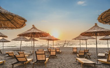 Gün batımı gökyüzü ve deniz altyapısı olan güneşli plaj şemsiyeleri. Sarande, Arnavutluk . 
