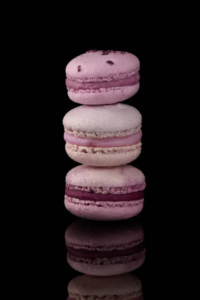 Pink and purple macarons cakes. Small French cakes. Sweet and colorful french macaroons. On black background.