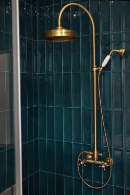 Yeni, zarif bir banyoda bronz duş başlığı ve cyan fayanslı duvara karşı musluk. Klasik tasarım