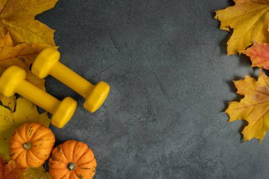 Şükran Günü veya Cadılar Bayramı için sonbahar kompozisyonu. Dambıl, balkabağı, kabak ve kabak yaprakları. Sağlıklı fitness yaşam tarzı konsepti. Beden eğitimi spor antrenmanı düzlüğü fotokopi alanı ile yatıyordu.