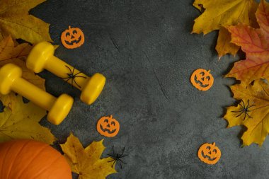 Cadılar Bayramı süslemeleri ve sonbahar balkabağı yapraklı iki sarı dambıl. Sağlıklı fitness yaşam tarzı kompozisyonu. Beden eğitimi ve spor eğitimi düz konsept fotokopi alanı ile.