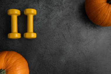 İki sarı dambıl ve turuncu balkabağı. Sağlıklı fitness yaşam tarzı sonbaharı ya da Cadılar Bayramı ya da Şükran Günü için düz kompozisyon. Kopya alanı ile spor ve eğitim kavramı.
