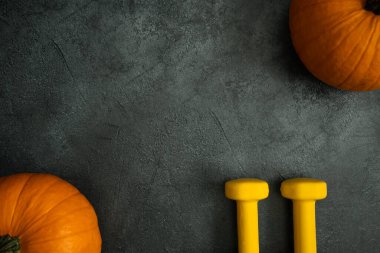 İki sarı dambıl ve turuncu balkabağı. Sağlıklı fitness yaşam tarzı sonbaharı ya da Cadılar Bayramı ya da Şükran Günü için düz kompozisyon. Kopya alanı ile spor ve eğitim kavramı.