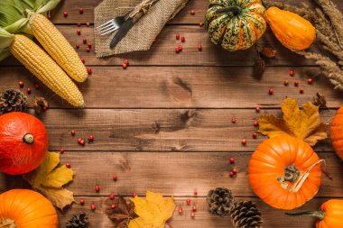 Autumn flat lay composition frame with copy space on wooden background. Pumpkins, cones, leaves, corn on the cob, with fork and knife on a jute material, for Thanksgiving dinner.