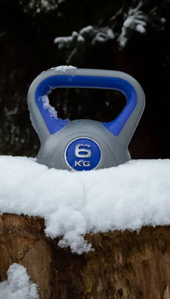 Kettlebell weight in a snow. Strength training fitness kettlebells. Heavy equipment for home gym workout, exercise in cold weather. Kettle bell with grip handle. Healthy lifestyle winter composition.