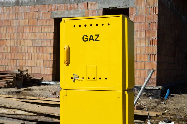 Yellow metal gas connection box at the construction site of a new single-family house. Unfinished stand-alone home building under construction. Letters in Polish language, Gaz means Gas.