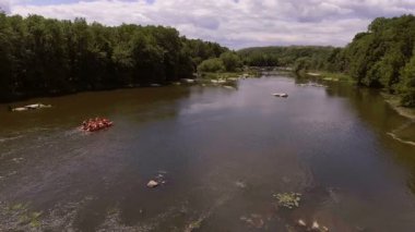 Akıntılı Manzaralı Nehirde Rafting Grubu. Parçalı bulutlu bir gökyüzü altında, yemyeşil ormanlar ve doğal güzelliklerle çevrili, yumuşak akıntılı bir nehirde rafting yapan insanların dinamik bir sahnesi..