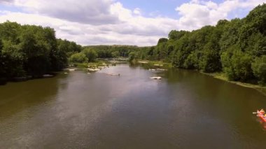 Akıntılı Manzaralı Nehirde Rafting Grubu. Parçalı bulutlu bir gökyüzü altında, yemyeşil ormanlar ve doğal güzelliklerle çevrili, yumuşak akıntılı bir nehirde rafting yapan insanların dinamik bir sahnesi..