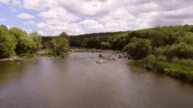 Akıntılı Manzaralı Nehirde Rafting Grubu. Parçalı bulutlu bir gökyüzü altında, yemyeşil ormanlar ve doğal güzelliklerle çevrili, yumuşak akıntılı bir nehirde rafting yapan insanların dinamik bir sahnesi..