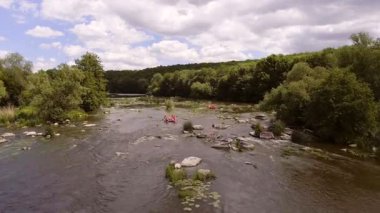 Akıntılı Manzaralı Nehirde Rafting Grubu. Parçalı bulutlu bir gökyüzü altında, yemyeşil ormanlar ve doğal güzelliklerle çevrili, yumuşak akıntılı bir nehirde rafting yapan insanların dinamik bir sahnesi..
