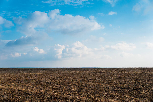 A plowed field on the background of a blue sky with clouds.