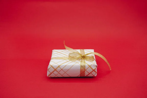 Small white gift box with gold ribbon. Christmas gift box. Isolated on a red background.