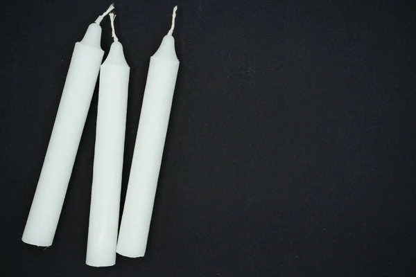 Three white wax candles on a black background. Long wax candles. New white wax candles.