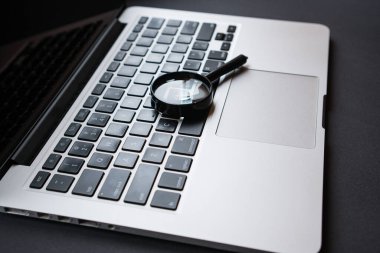 Karanlık ofis masasında büyüteçli dizüstü bilgisayar, arama ve analiz konsepti.