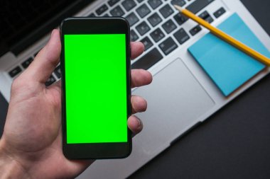 Green Chroma Key Screen ile Man Holding Smartphone, arka planda modern işyeri.