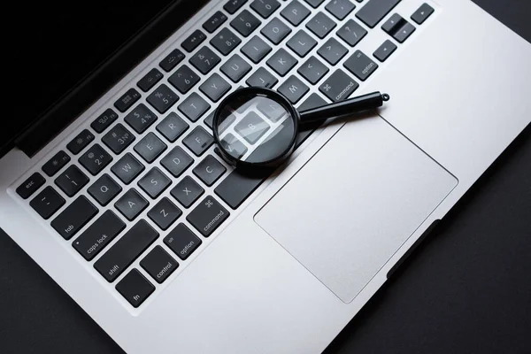 stock image Laptop with magnifying glass, on dark office table, concept of search.