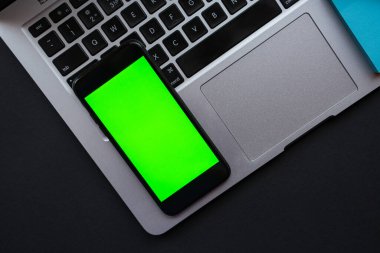 Ofis işyeri, ahşap masa üzerinde dizüstü bilgisayar ve cep telefonu dikey yeşil ekran, üst görünüm, düz yatış.