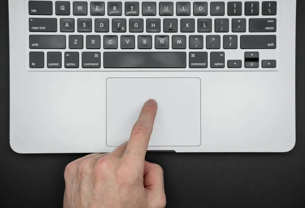 A man uses a laptop. The finger points to the touchpad. Close up top view.