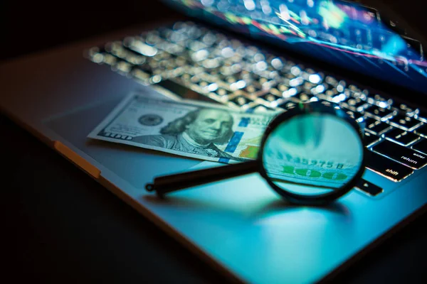 Concept of money market, financial economy. Magnifying glass and dollar bills on laptop. Shallow depth of field.
