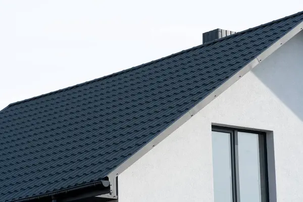 The dark-colored roof of a new residential house. Roof covering with steel tiles.