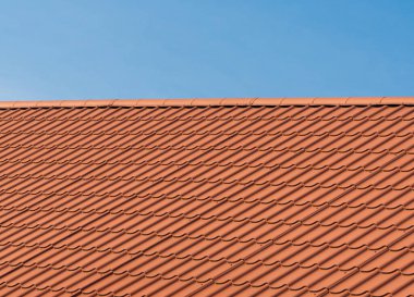 Roof with orange tiles on a background of blue sky. Shingles texture. New roof.