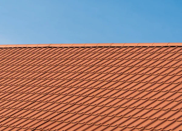 Roof with orange tiles on a background of blue sky. Shingles texture. New roof.