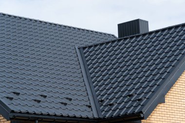 Evin çatısı yeni siyah metal fayanslarla kaplı. Metalden yapılmış modern çatı. Modern yapı.