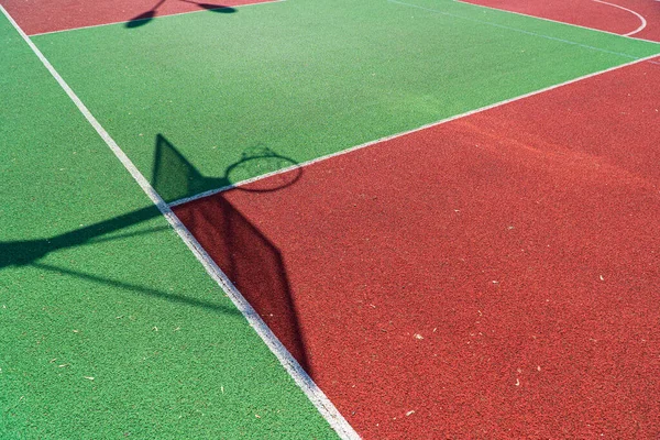 Shadow of the rack with shield and basketball ring on basketball field. Colorful basketball lines on an outdoor court.