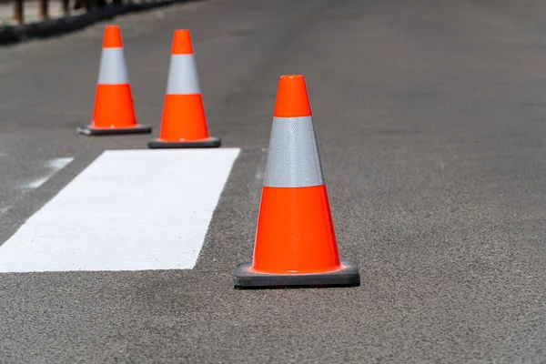 Orange construction cones on an asphalt road. Newly painted striped road markings of a pedestrian crossing.