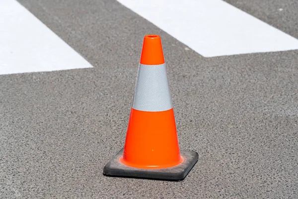 Traffic cone, with white and orange stripes on gray asphalt. Construction cone. Symbol of restrictions, roadworks, attention.