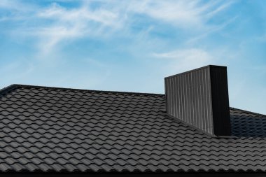 Evin çatısı gökyüzüne karşı siyah metal modern çatı malzemesi ile kaplı. Oluklu metal çatı ve metal çatı..