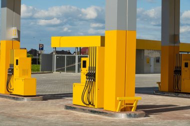 Parlak sarı yakıt pompaları yeni açılan bir benzin istasyonunda duruyor. Üzerinde mavi bir gökyüzü var. Alan geniş ve aydınlık, temiz ve modern bir görünüm sunuyor..