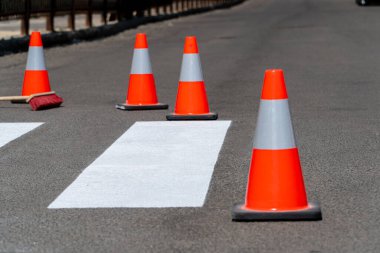 Parlak turuncu trafik konileri yeni işaretlenmiş bir yaya geçidi boyunca yayaları yöneten ve bölgede güvenliği sağlayan bir yaya geçidi boyunca yerleştiriliyor..