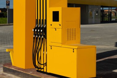 Yakıt pompası belirgin bir şekilde bir benzin istasyonunda duruyor, çarpıcı sarı desenli çoklu dağıtıcılar, açık mavi gökyüzü ve yeşil çevreye karşı dizilmiş.