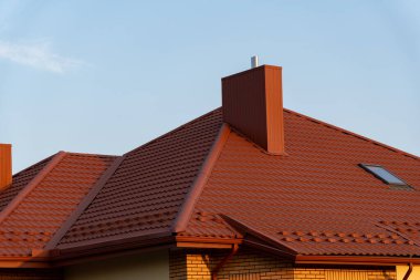 The vibrant red roof structure features a prominent chimney and an angled design, bathed in warm afternoon light against a clear blue sky, highlighting its architectural details. clipart