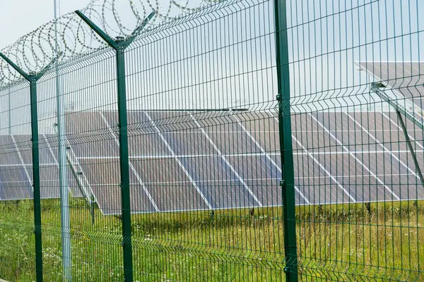 Güneş panelleri, dikenli tellerle kaplı yeşil bir çitin yer aldığı güvenli bir alana monte edilir ve yenilenebilir enerjiye olan bağlılığını gösterir..
