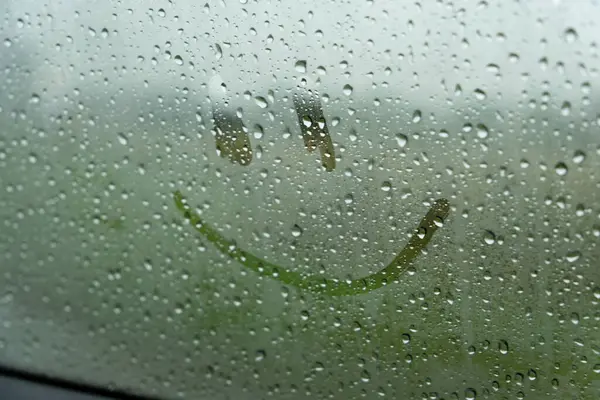 Arabanın camına tek bir gülen yüz çizilir. Pencere yağmur damlalarıyla kaplı, dışarıdaki manzarayı engelliyor. Gülen yüz su damlacıklarından görülebiliyor..