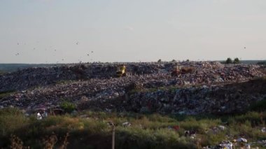 Atık yönetiminin zorluklarını vurgulayarak, geniş bir çöp sahasında ağır makineler çalışıyor. Çamur geniş bir gökyüzünün altında etrafa saçılmış.