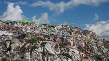 Plastik ve tekstil de dahil olmak üzere enkaz dağları içeren parlak mavi gökyüzünün altında büyük bir atık alanı görülebilir. Olay yeri, acil çevresel kaygıların altını çiziyor. 4k görüntü.
