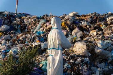 Koruyucu dişli anketlerine adanmış bir birey, atık sahasındaki yüksek bir çöp yığınını inceleyerek, sürdürülebilir atık yönetimi uygulamaları ve çevresel sorumluluklara duyulan acil ihtiyacı vurguluyor.