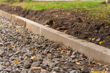 Bu sakin ortamda, yeni bir çakıl yolu ortaya çıkar, sağlam beton bir kaldırım tarafından titizlikle kenarlı, titreşen yapraklar yere saçılırken, keşifleri davet ederek.