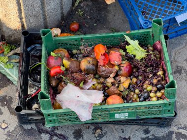 A crate filled with decomposing fruits and vegetables lies discarded on the ground. This illustrates the issue of food waste, typically found at market cleanup times. clipart