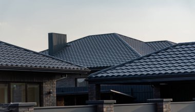 Çağdaş bir evin çatısı, güneş ışığını yansıtan ve konut mimarisindeki modern inşaat tekniklerini vurgulayan şık siyah metal fayanslar sergiliyor..