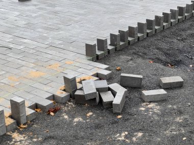 İşçiler kaldırımı onarmak için çakıl zemine taş döşüyorlar. Yakınlarda da bazı taşlar var. Bu da devam eden inşaatı gösteriyor..