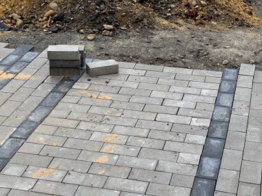 Kaldırımın bir kısmı gri kaldırım taşlarıyla onarılıyor. Sıraya dizilmiş birkaç taş var, ama bölgenin çoğu hala çıplak..