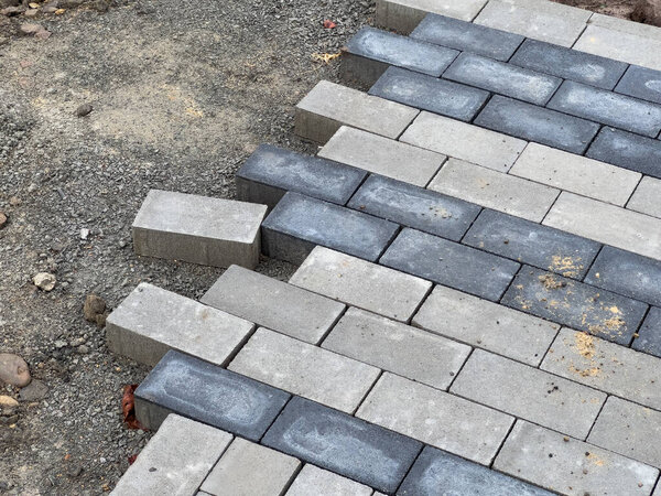 Рабочие тщательно выкладывают камни на фундамент из гравия, продвигаясь через проект по ремонту тротуаров в этом жилом районе.