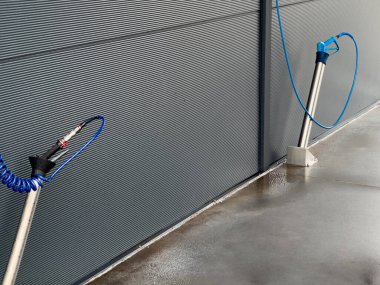 İki yüksek basınçlı oto yıkama tabancası gri bir duvara dayalı, iyi aydınlatılmış bir otomotiv servisinde araçları etkili bir şekilde temizlemek için donanımlı..