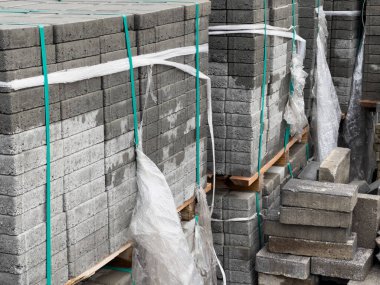 Birden fazla gri kaldırım taşı yığını plastik ambalajla düzgünce düzenlenmiş. Taşımacılık için hazırlar, peyzaj ya da yol yapım projelerinde kullanılmayı bekliyorlar.